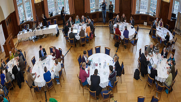 In einem Saal sitzende Personen bei Diskussionen an runden Tischen bei einer Veranstaltung zum Wettbewerb für vorbildliche Bürgerbeteiligung